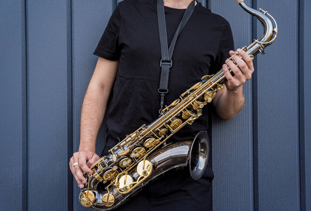 Young street musician playing saxophone near the big blue wall - Zdjęcie, obraz