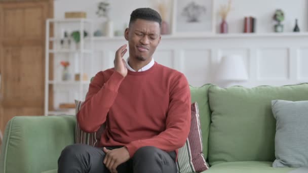 Африканский мужчина испытывает боль в шее, сидя на софе  - Кадры, видео