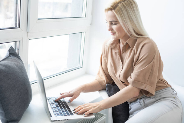 Miła piękna blondynka pracuje w notebooku usiąść na kanapie w domu - sprawdź na oline sklepy dla cyber sprzedaży poniedziałek - technologia kobieta koncepcja alternatywnego biura freelance - Zdjęcie, obraz