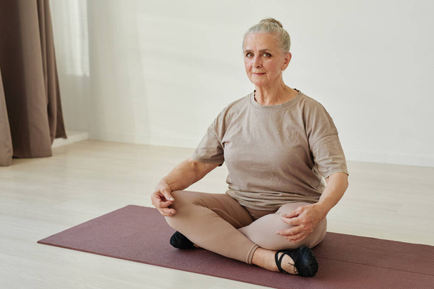 Contemporary senior female in activewear sitting in lotus position on mat - Foto, Bild