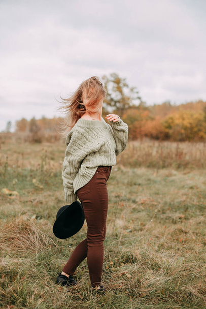 Portrait of a young blonde girl in a green sweater and brown jeans in a field in autumn - Foto, Bild