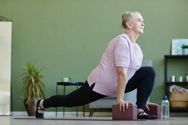 Ενεργό ηλικιωμένη γυναίκα με γιόγκα μπλοκ άσκηση στο πάτωμα - Φωτογραφία, εικόνα