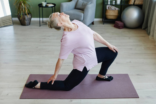 Oudere grijs-harige vrouw kijkt omhoog tijdens yoga oefening - Foto, afbeelding