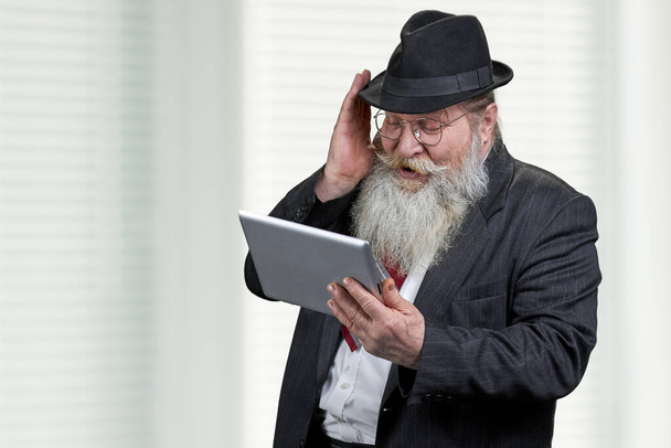 Velho empresário sênior olhando para tablet digital pc com expressão surpresa. - Foto, Imagem