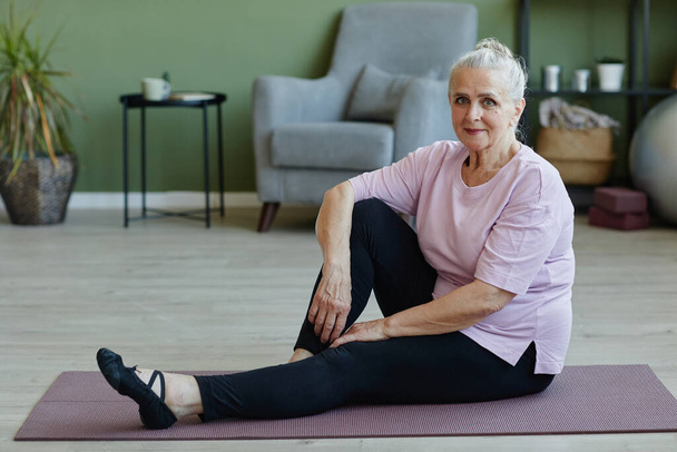 Gelukkig senior vrouw in sport kleding zittend op yoga mat - Foto, afbeelding