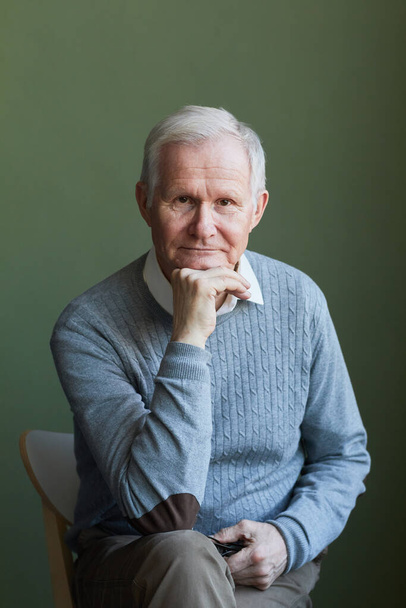 Serious elderly man in light blue pullover sitting on chair - Photo, Image
