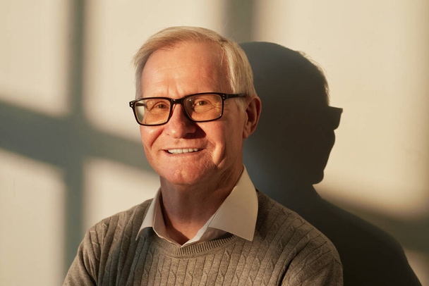 Fröhlicher älterer Mann mit Brille und lässigem Pullover steht an der Wand - Foto, Bild