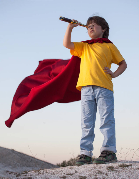 Boy playing superheroes on the sky background, teenage superhero in a red cloak on a hill - Foto, afbeelding