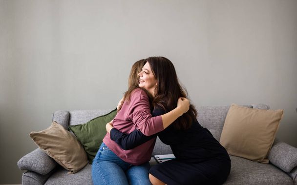 Ψυχολογική βοήθεια στις γυναίκες. Δύο γυναίκες κάθονται στον καναπέ και αγκαλιάζονται. Υποστηρικτικές αγκαλιές - Φωτογραφία, εικόνα