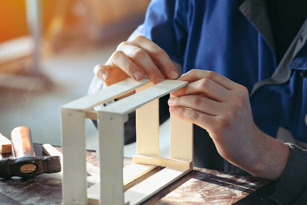 Jeune menuisier caucasien en vêtements de travail fait des boîtes en bois dans l'atelier de menuiserie. Une vraie scène. Petites entreprises - Photo, image