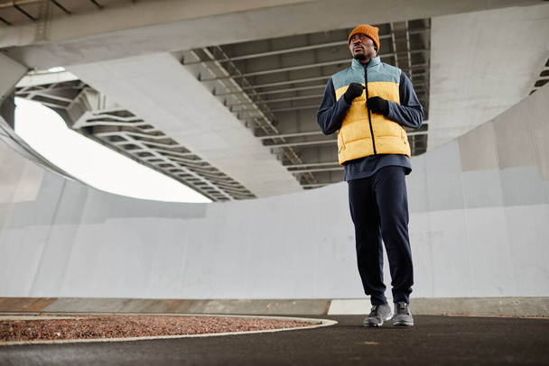 Mladý aktivní afroameričan muž v teplém sportovním oblečení běží dolů jogging track - Fotografie, Obrázek