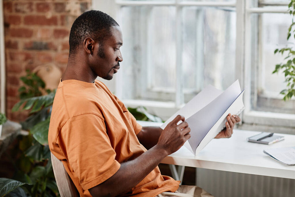 Side view of young African American businessman looking through financial papers - Φωτογραφία, εικόνα