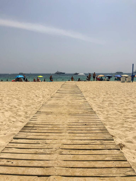 Drewniana promenada w środku piaszczystej plaży z turkusowym oceanem i wczasowiczami pod błękitnym niebem - Zdjęcie, obraz