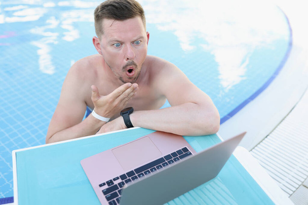 Joven sorprendido en la piscina mira en un ordenador portátil - Foto, imagen