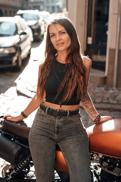 Femme aux cheveux bruns posant avec une moto rétro urbaine sur l'allée - Photo, image