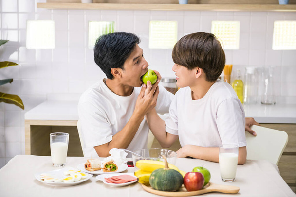 Aranyos ázsiai LMBT meleg fiatalember etetni zöld almát a partnere, miközben eszik szendvicset és salátát otthon. Ugyanaz a szex család reggelizik.. - Fotó, kép