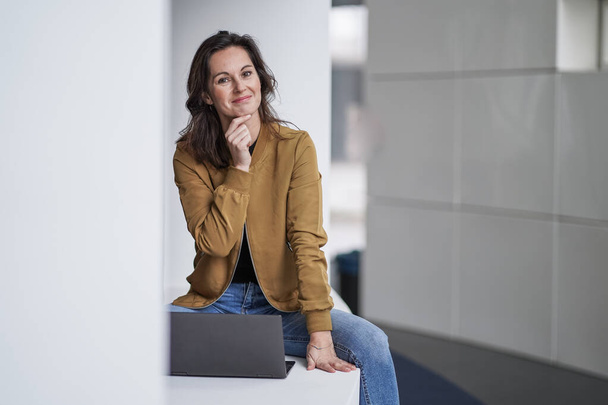 happy beautiful student woman working remotely infront of a notebook in casual jeans outfit in a modern university lobby on a white background - Fotó, kép