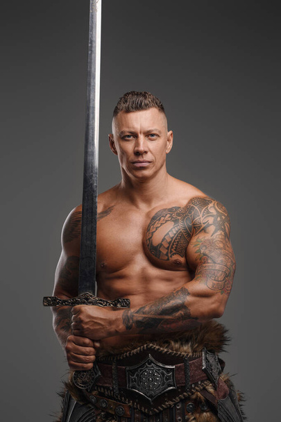 Muscular warrior with naked torso holding sword against gray background - Photo, Image