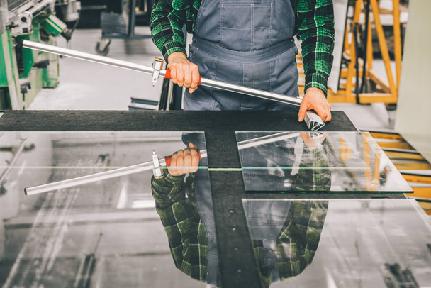 Vidriero de pie sobre un panel de vidrio cortado con equipos de corte especializados, paneles de vidrio de corte en la fábrica  - Foto, imagen