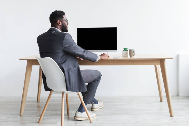 Czarny biznesmen w formalnym stroju siedzi przy stole, pracuje z komputerem, makieta do projektowania stron internetowych - Zdjęcie, obraz