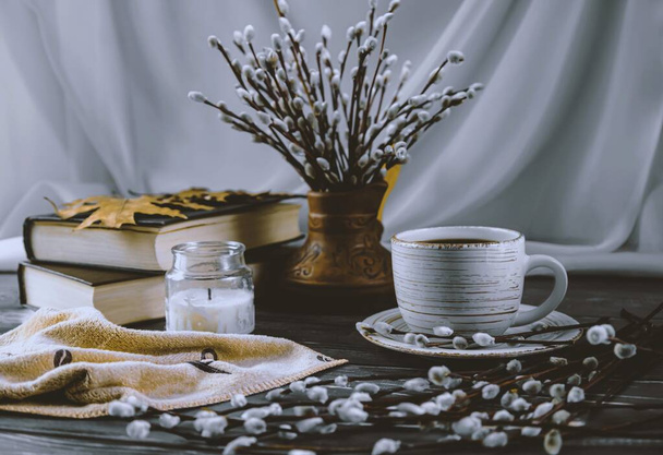 Ramitas de sauce, taza de café, libros y velas. Bodegón de primavera sobre fondo blanco y madera. Vista lateral. - Foto, imagen