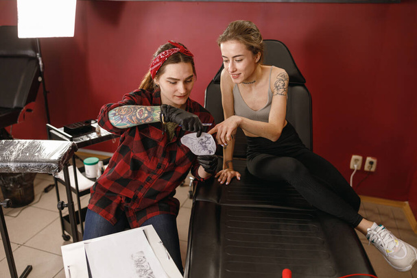 Καλλιτέχνης τατουάζ δείχνει το σχέδιο πελάτη για τατουάζ - Φωτογραφία, εικόνα