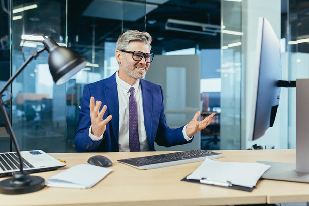 Angry and upset boss businessman shouting at computer monitor, man with glasses working in modern office at computer - Foto, Bild