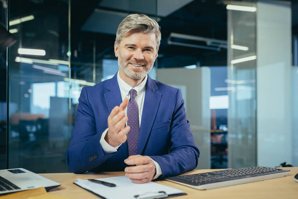 An experienced manager looks at the camera and smiles, a businessman claps his hands on a video call, as a sign of praise and support to interlocutors - Fotoğraf, Görsel