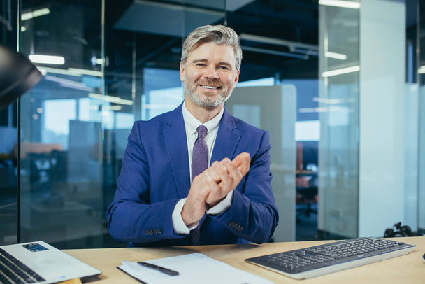 An experienced manager looks at the camera and smiles, a businessman claps his hands on a video call, as a sign of praise and support to interlocutors - Fotoğraf, Görsel