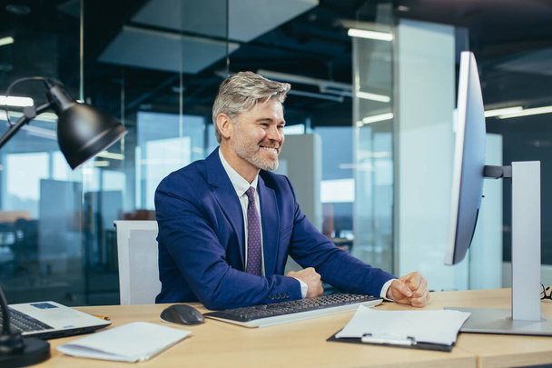 Portrait of a successful experienced gray-haired broker man, business man working in a modern office, looking at the camera rejoices and smiles - Foto, Bild