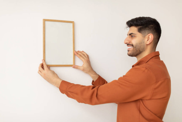 Retrato de porrista hombre colgando marco de fotos en la pared - Foto, Imagen