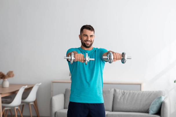 alegre millennial musculoso europeo chico haciendo ejercicios de brazo, levanta pesas, entrenamiento para bíceps - Foto, imagen