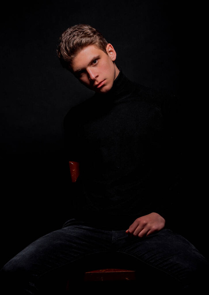 Studio fashion portrait of a young man wearing long-sleeve shirt sitting on cheir - Foto, immagini
