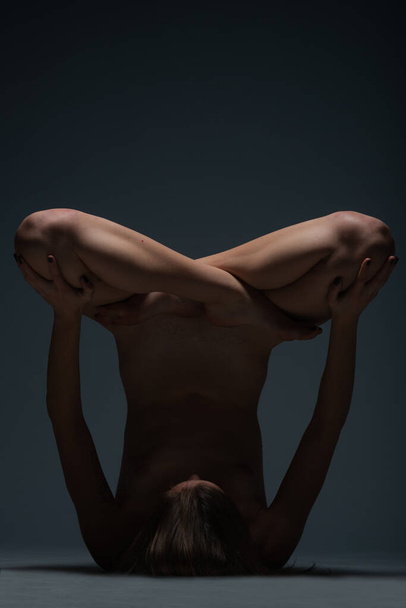 A testa in giù foto acrobatica di una giovane donna nuda sdraiata sul pavimento in uno studio buio - Foto, immagini