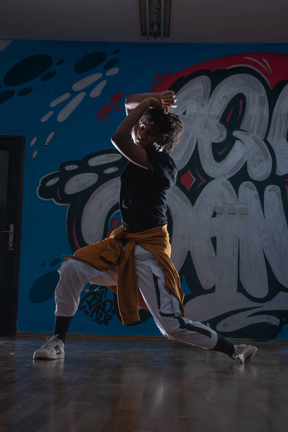 Jonge zwarte man dansend hip hop stijl in een stedelijke omgeving. hij draagt een oranje outfit en heeft een graffiti achtergrond. - Foto, afbeelding