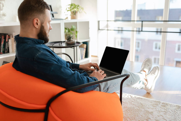 Homme indépendant utilisant un ordinateur portable avec écran vide assis à la maison - Photo, image