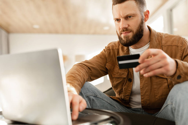 Человек с помощью ноутбука и кредитных карт покупки в Интернете сидя в помещении - Фото, изображение