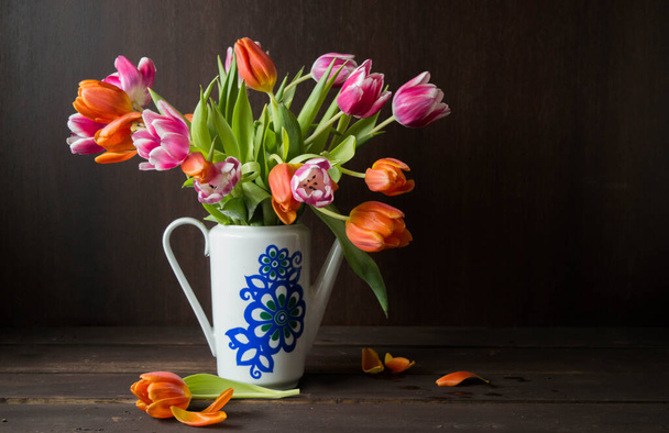 pink and orange colored tulips in vase in front of a dark brown wooden wall background - Фото, зображення
