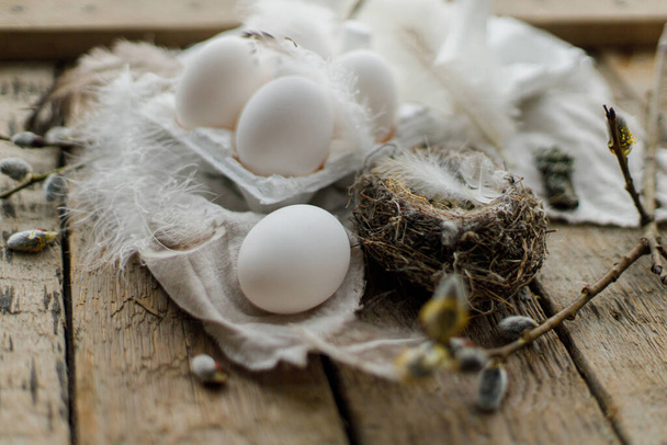 Πασχαλινά φυσικά αυγά σε δίσκο, φτερά, κλαδιά ιτιάς, φωλιά, λινό ύφασμα σε παλαιωμένο ξύλινο τραπέζι. Κομψή πασχαλινή ρουστίκ νεκρή φύση. Απλή αγροτική αισθητική. Καλό Πάσχα. - Φωτογραφία, εικόνα