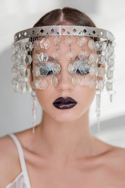 Fashion beauty close-up portrait of girl with black glossy lips, blue eyeshadows. The head is decorated with a crown made of transparent snow crystals, long silver earrings. Daring professional makeup - Valokuva, kuva