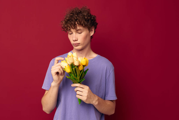 young guy holding a yellow bouquet of flowers purple t-shirts red background unaltered - Zdjęcie, obraz