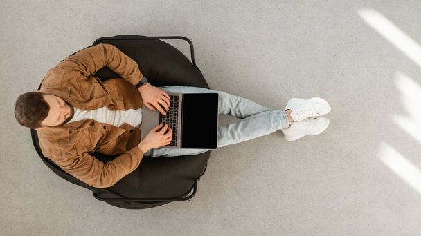 Masculino usando laptop com tela em branco sentado no interior, vista superior - Foto, Imagem