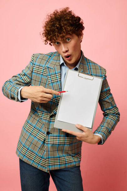 Young curly-haired man folder for papers blank sheet posing in suit pink background unaltered - Фото, зображення