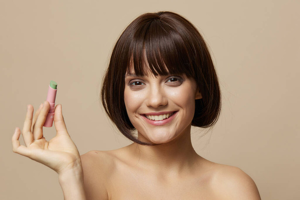 maquillaje de mujer joven brillo de labios cerca de la cara hombros desnudos fondo beige - Foto, Imagen