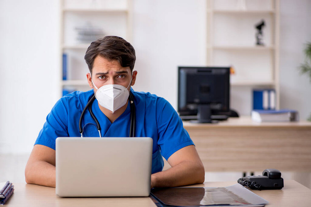 Молодой врач-мужчина работает в клинике во время пандемии - Фото, изображение