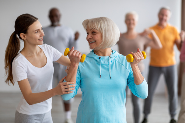 Vrouwelijke fitnesscoach helpt oudere vrouw tijdens het sporten - Foto, afbeelding