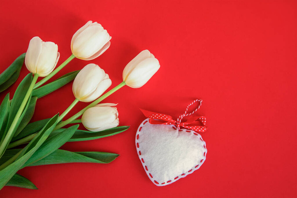 Tulipanes blancos y corazón de juguete sobre fondo rojo. Concepto de San Valentín. Vista superior, plano. - Foto, imagen