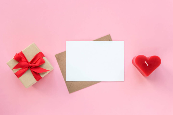 Gift box, envelope with blank card and red candle in a shape of heart on pink background. Valentines day concept. Top view, flat lay, mockup. - Foto, Bild