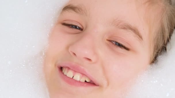 Portrait of cheerful teen girl lying in bath with thick soap foam and looking in camera. Concept of child hygiene and health care at home. Child having fun and playing at home - Footage, Video