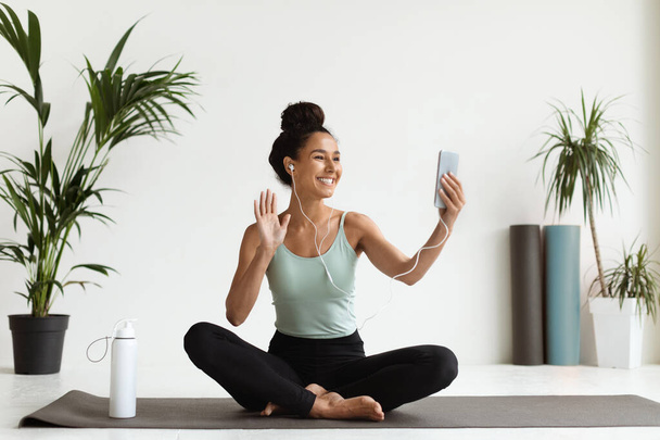 Усміхнена молода жінка зі смартфоном робить відео дзвінок з диваном йоги
 - Фото, зображення